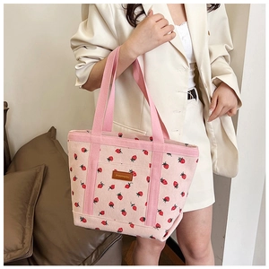 Detail of pink corduroy tote bag featuring red strawberry patterns and a leather logo