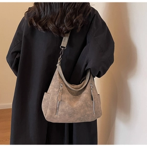 Rear view of a taupe hobo bag in matte synthetic leather styled with a black trench coat