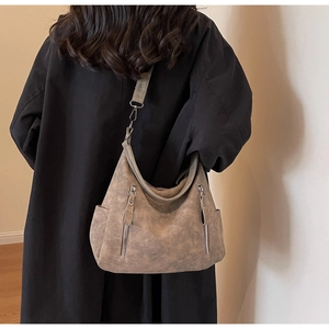 Detail of large khaki crossbody tote bag with vertical zippers on model in black coat