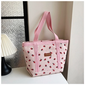 Detailed close-up of pink corduroy tote bag featuring red strawberry patterns and leather patch