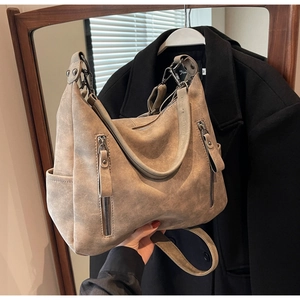 Detail of camel suede tote bag with metal zippers and side pocket on black coat background