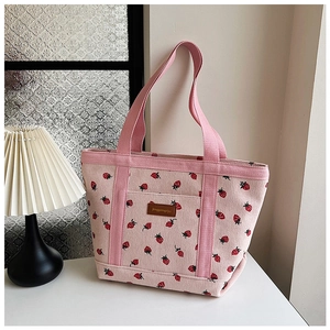 Detail of pink corduroy tote bag featuring red strawberry prints and leather logo patch