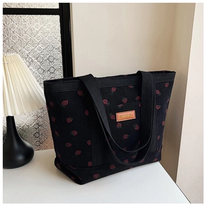 Detail of black corduroy tote bag featuring red strawberry prints and leather label
