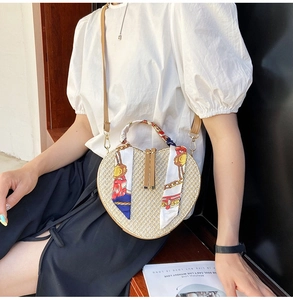 Detail of heart-shaped woven straw bag with colorful silk scarves and brown leather strap