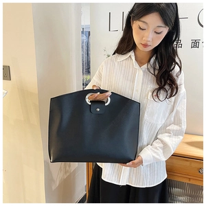 Detail of minimalist black PU leather tote bag with elegant silver round metal handle