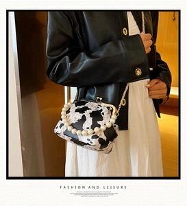 Detail of cow print crossbody bag with gold clasp and pearl handle on a model
