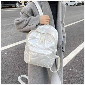 Sac à dos matelassé blanc porté avec un manteau gris dans un cadre urbain moderne