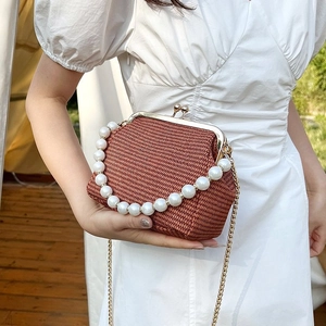 Vintage brown woven shell bag with pearl handle and gold chain strap in outdoor setting