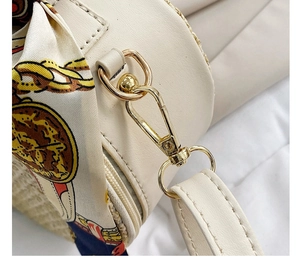 Close-up of golden hardware hooks and a vintage chain print silk scarf on a beige woven bag