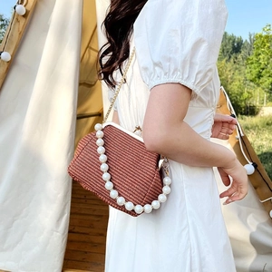Detail view of woven brown crossbody bag with pearl handle and metal chain strap