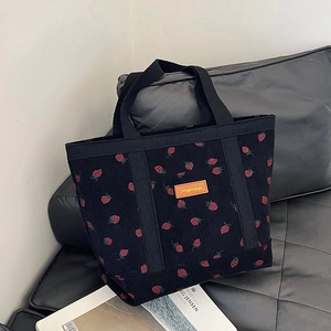 Corduroy tote bag with strawberry print and orange label on a black leather sofa