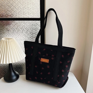 Black corduroy tote bag with red strawberry print and leather label on white surface