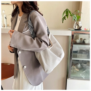 Detail of off-white corduroy tote bag featuring striped shoulder strap in a cafe