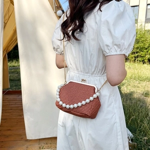 Detail of a brown woven mini bag with pearl handle and golden chain on a white dress