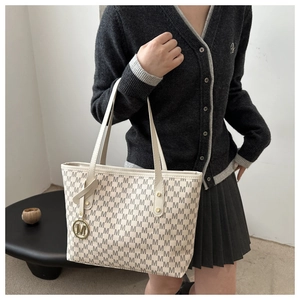 Close-up of off-white tote bag with letter print, golden charm, and slim shoulder strap