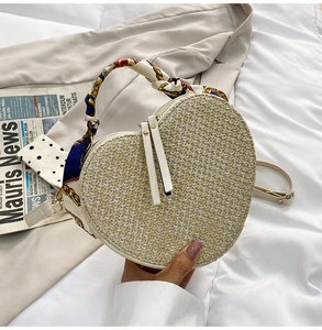 Detail of heart-shaped woven straw handbag with decorative silk scarf handle and dual zippers
