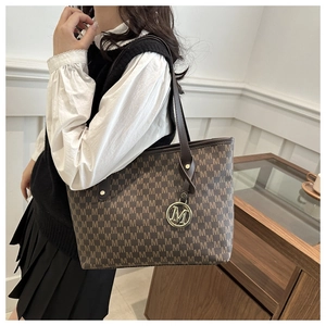 Detail of large brown tote bag with M-pattern texture and metal pendant on model