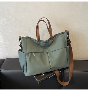 Dettaglio della borsa tote in nylon verde salvia con manici in pelle sul divano
