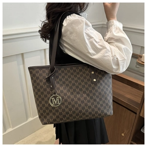 Detailed close-up of brown monogram tote bag featuring golden M-letter metal pendant