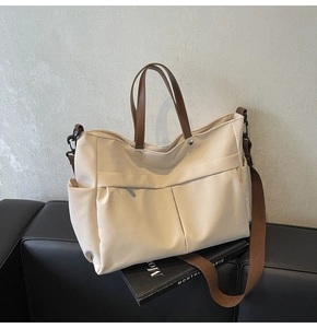 Dettaglio borsa tote in nylon crema con manici in pelle marrone su panca in pelle nera