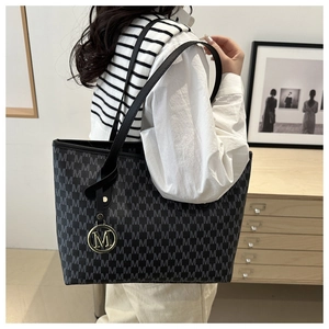 Detailed view of the large grey tote bag with M-pattern print and metallic charm