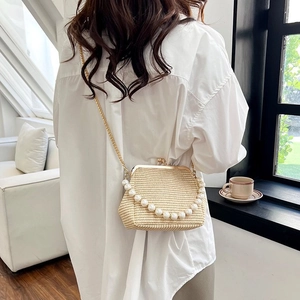 Detail of a beige straw woven bag with pearl handle and golden chain shoulder strap