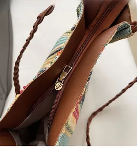 Close-up of the smooth metal zipper and brown PU leather trim on the striped woven tote bag