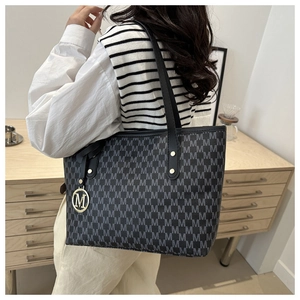 Detailed view of large tote bag featuring monogram pattern and gold M metal pendant