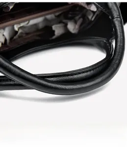 Detail view of black leather tote bag showing handle stitching and zipper closure