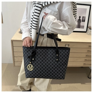 Close-up of printed monogram pattern and gold M-letter metal pendant on black tote bag