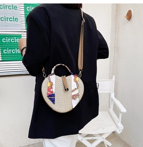 Close-up of heart-shaped woven straw shoulder bag with decorative silk scarf on model