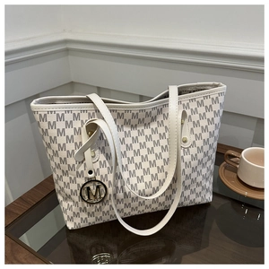 Detail of a cream tote bag with dark grey 'M' pattern and gold metallic charm