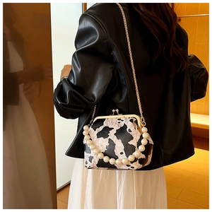 Close-up of vintage cow print shell bag with pearl handle and gold chain strap