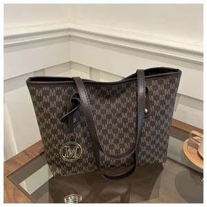 Macro detail of brown monogram tote bag with gold metal M-shaped logo charm