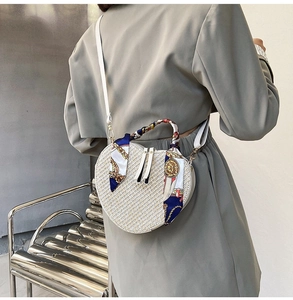 Detail of a white heart-shaped woven bag with ribbon handle and leather strap on a model