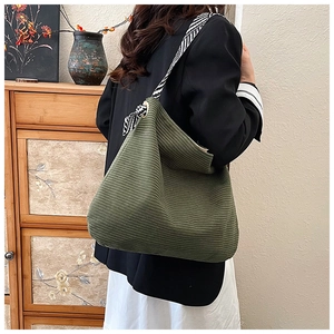 Detail of dark green corduroy tote bag with woven checkerboard strap worn by a model