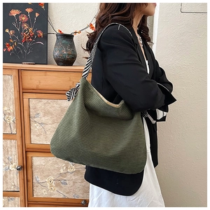 Olive green corduroy tote bag detail with striped strap shown on a model in a cozy setting