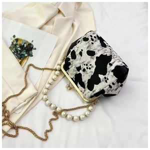 Detail of cow print mini frame bag with pearl handle and golden chain on white fabric