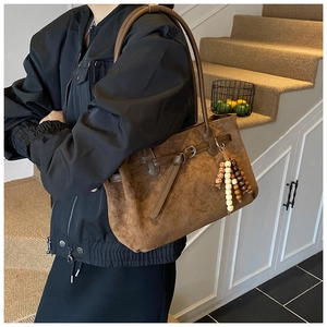 Borsa tote in camoscio marrone con ciondolo in legno indossata da una modella