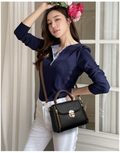 Detail of black pebbled leather crossbody bag with brown handle and golden round lock