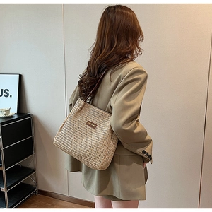 Detail of woven straw tote bag featuring brown leather handles and a minimalist texture