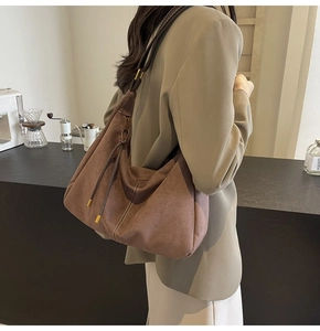 Brown suede hobo bag with contrast stitching shown on shoulder in a cafe setting