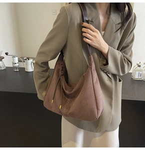 Close-up of brown suede hobo bag with wide leather strap and decorative fringe details