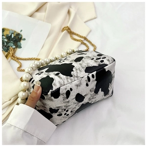 Detail of faux leather crossbody bag featuring black cow print and gold pearl chain strap