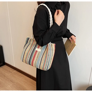 Detail of colorful striped woven tote bag with white braided handles on a model
