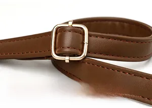 Macro view of adjustable dark brown leather shoulder strap with gold metal buckle