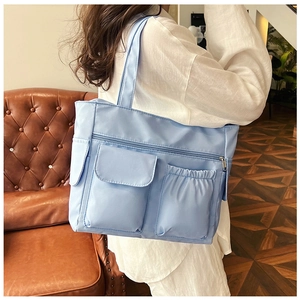 Detail of light blue nylon tote bag with multiple pockets shown on model's shoulder