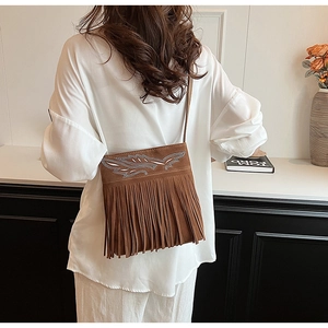 Detail of bohemian brown suede crossbody bag featuring long fringe and silver feather inlay