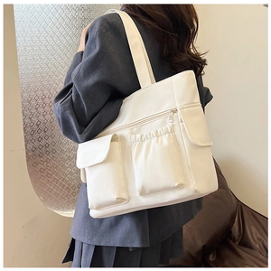 Detail of white multi-pocket tote bag showing the flap and drawstring storage compartments