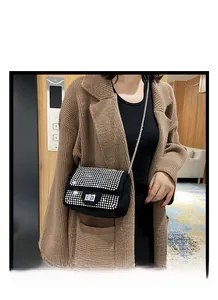 Elegante borsa a patta nera con strass e catena d'argento indossata su un maglione marrone